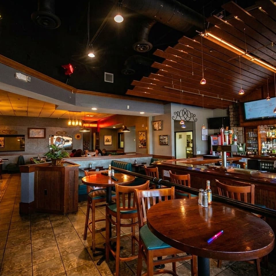 A restaurant interior with a full bar, high-top tables, and booth seating under warm lighting.