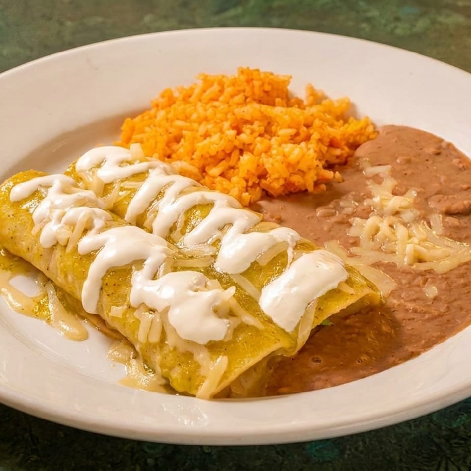 Two green enchiladas topped with sour cream and cheese, served with rice and refried beans.