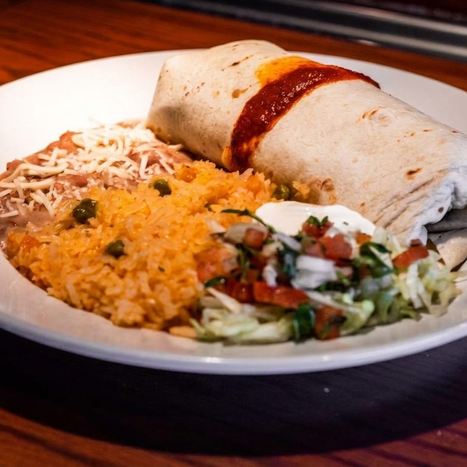 A large burrito topped with red sauce, served with rice, refried beans, and a side salad.