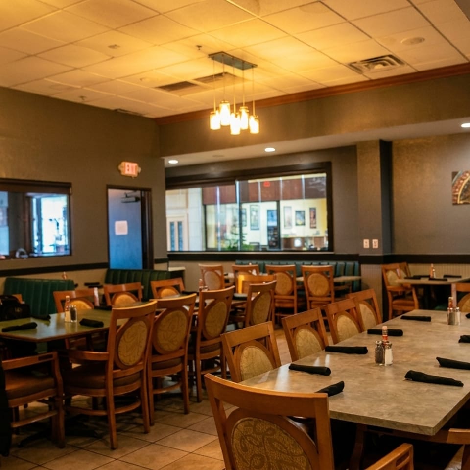 Empty restaurant dining room with green booths, wooden chairs, and tables set for service.