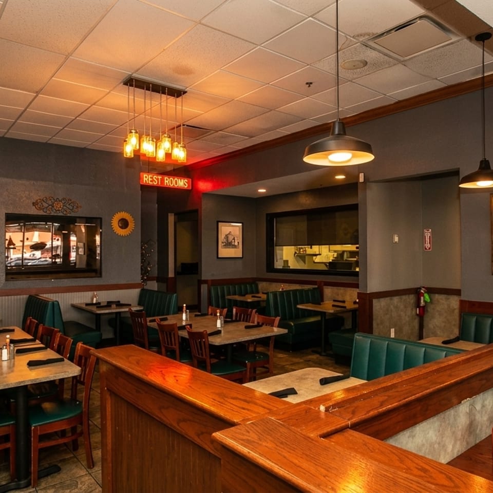 Restaurant interior with green booths, wooden tables, and a "Rest Rooms" neon sign.