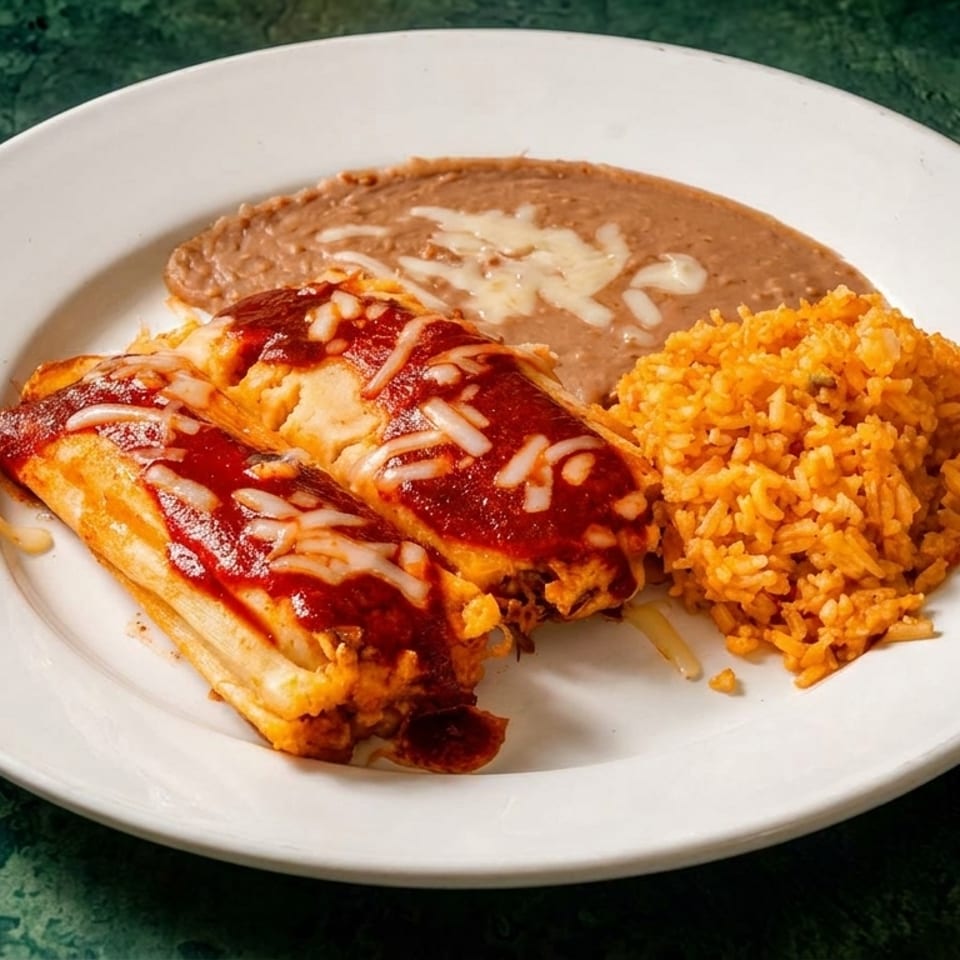 Two tamales topped with red sauce and cheese, served with refried beans and Spanish rice.